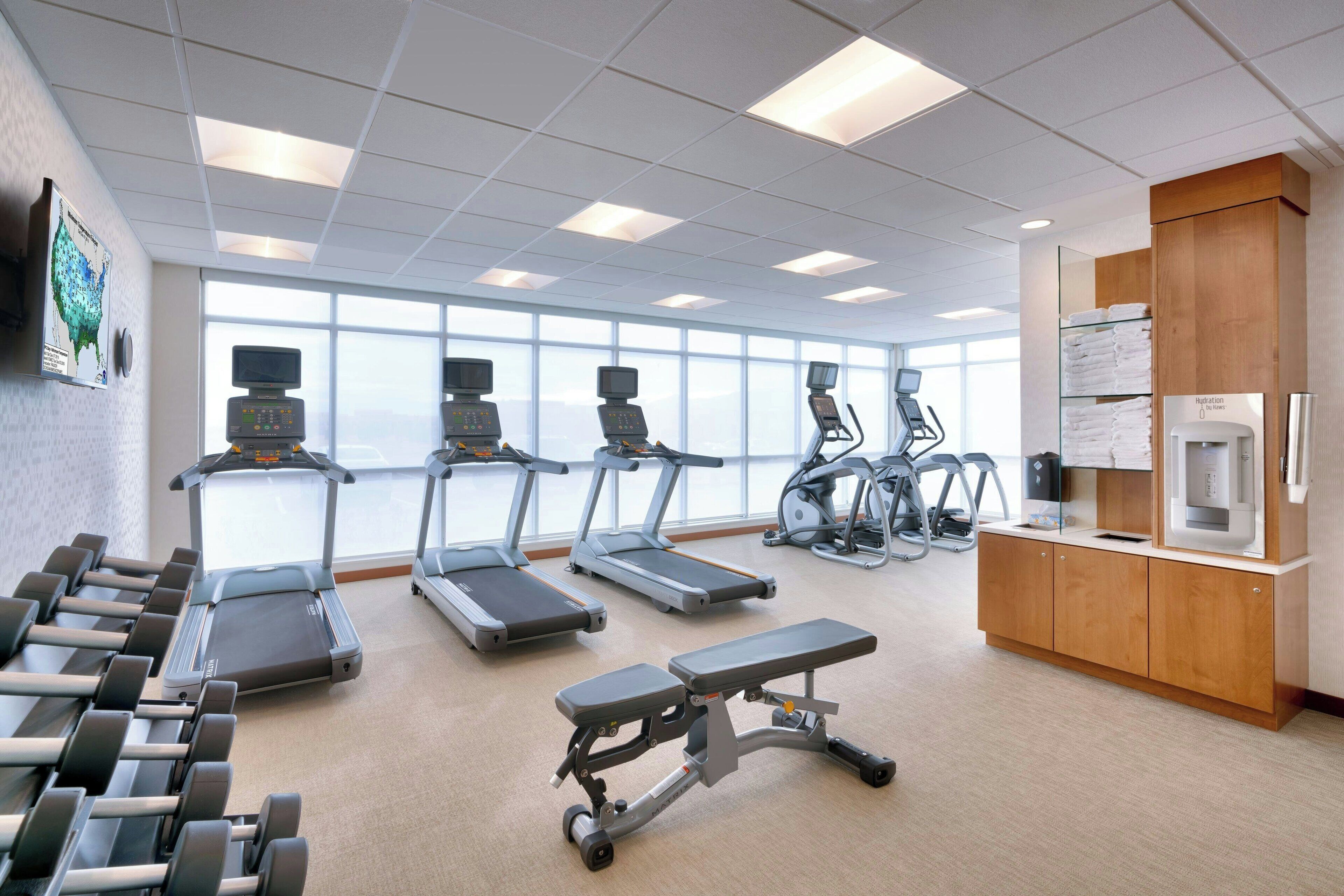 A gym with treadmills, dumbbells, and a bench.