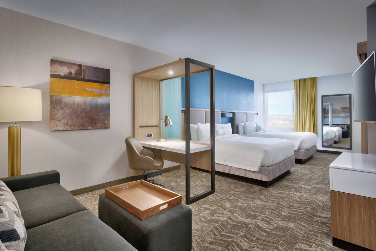 Ein Hotelzimmer mit Schreibtisch, zwei Betten, einer Sitzecke und Blick auf die Stadt.