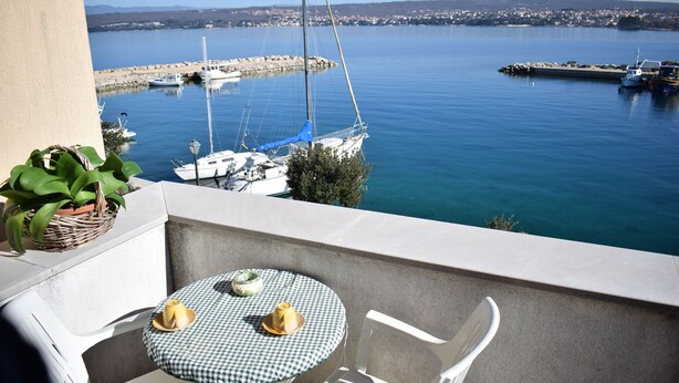 A balcony with a table and chairs, overlooking a marina with boats and a distant town. - Apartment Blue Dream 1 & 2 (Malinska-Dubasnica)