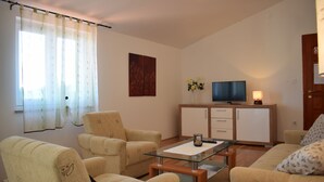 A living room with a sofa, armchairs, a glass coffee table, a TV on a cabinet, and a window with curtains. - Apartment Blue Dream 1 & 2 (Malinska-Dubasnica)