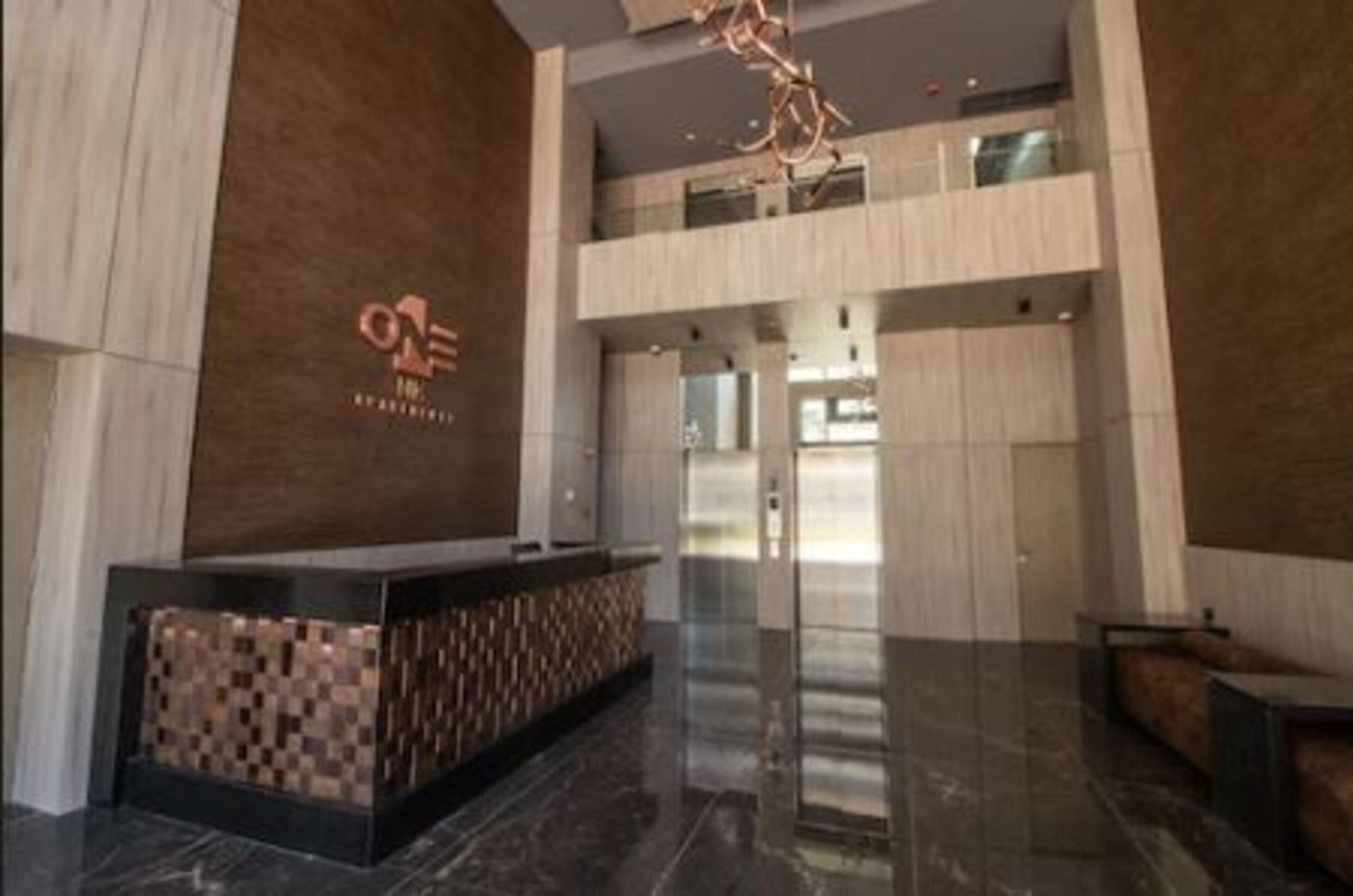A modern reception area with a check-in counter, a large chandelier, and a double-height ceiling.