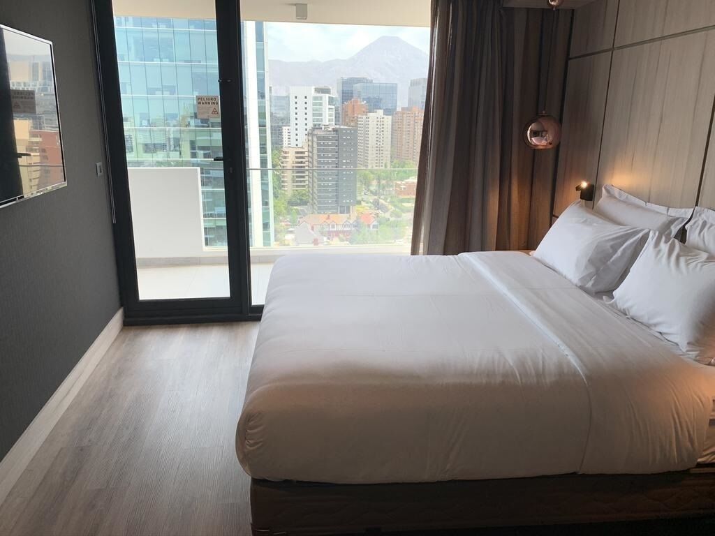 A hotel room with a large bed, a view of the cityscape, and a sliding glass door.