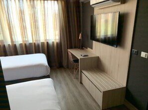 A hotel room with two beds, a desk, a chair, a TV, and an air conditioning unit. - One Nk Apartments (Santiago)
