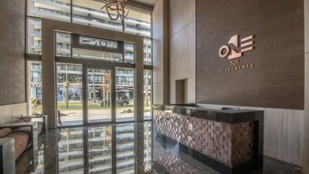 A modern hotel lobby with a reception desk, large windows, and a view of the street. - One Nk Apartments (Santiago)