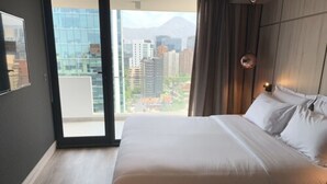 A modern hotel room with a large bed, a view of the city through a glass door, and a cityscape visible through the window. - One Nk Apartments (Santiago)