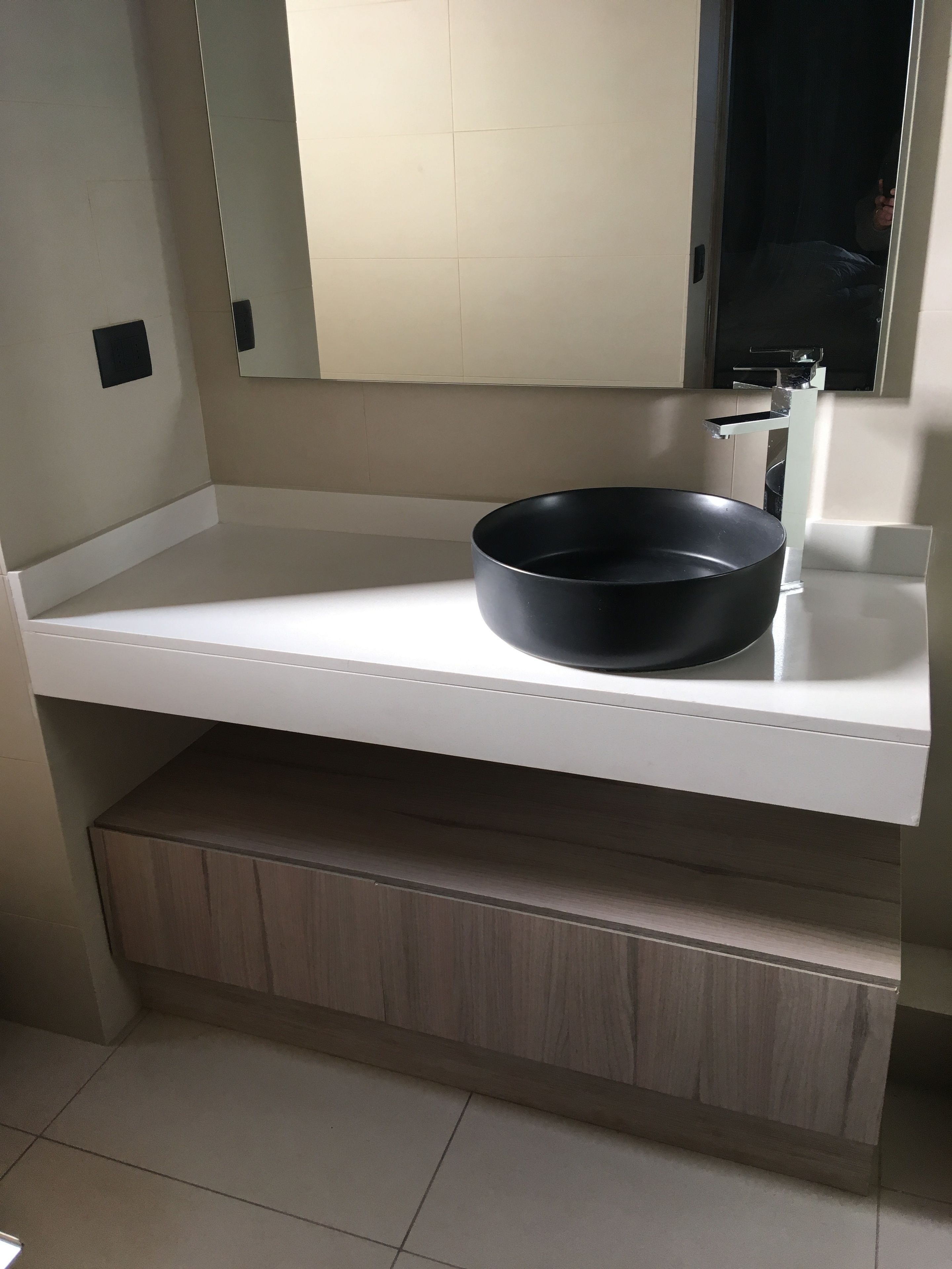 A bathroom with a white countertop, a black basin, and a mirror above the sink.