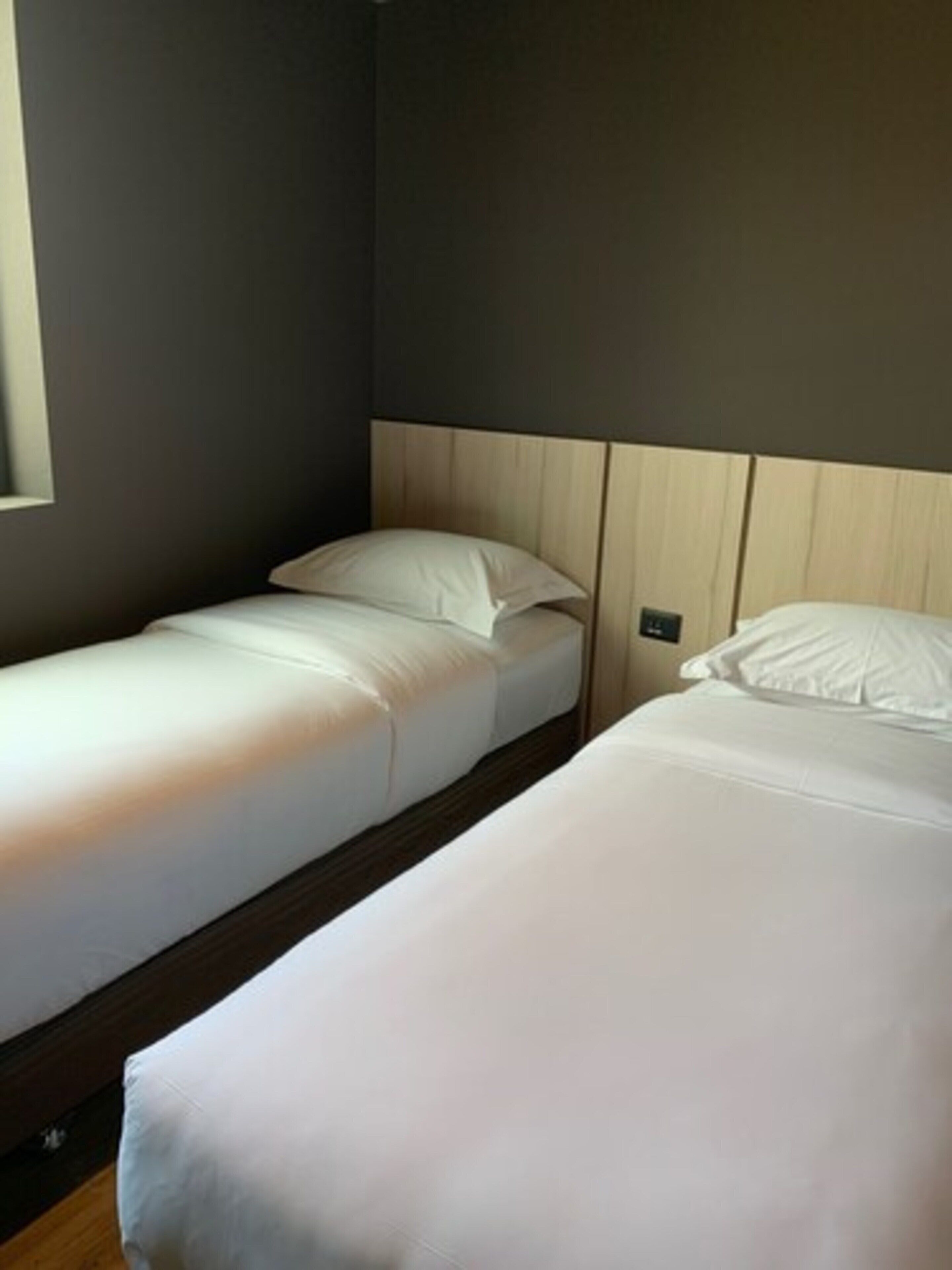 A room with two single beds, wooden headboards, and a small window.