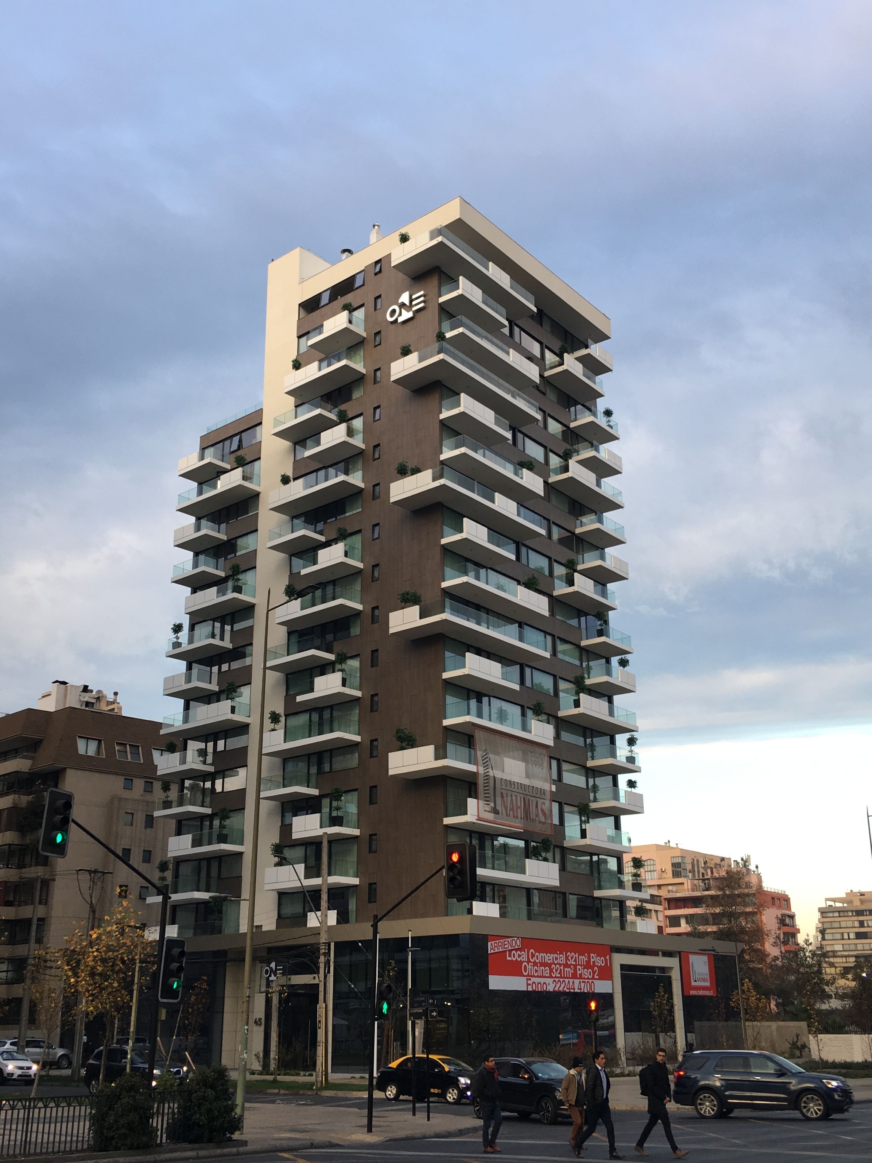 Un edificio de gran altura con varios balcones, un letrero comercial en la planta baja y un semáforo en primer plano.