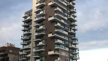 Un edificio de gran altura con varios balcones, un letrero comercial en la planta baja y un semáforo en primer plano.