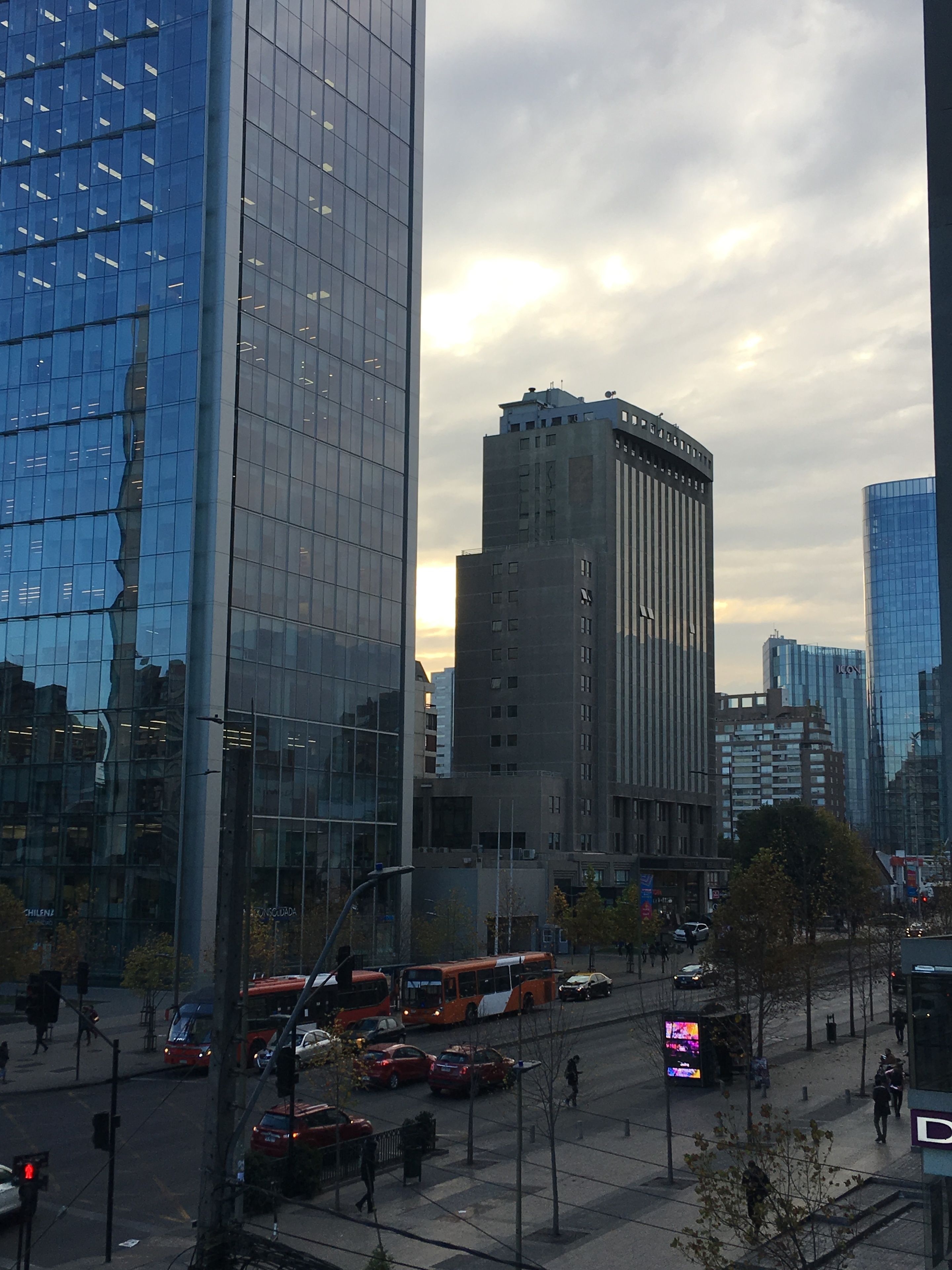 A cityscape with modern buildings, a busy street with cars and buses, and a clear sky.