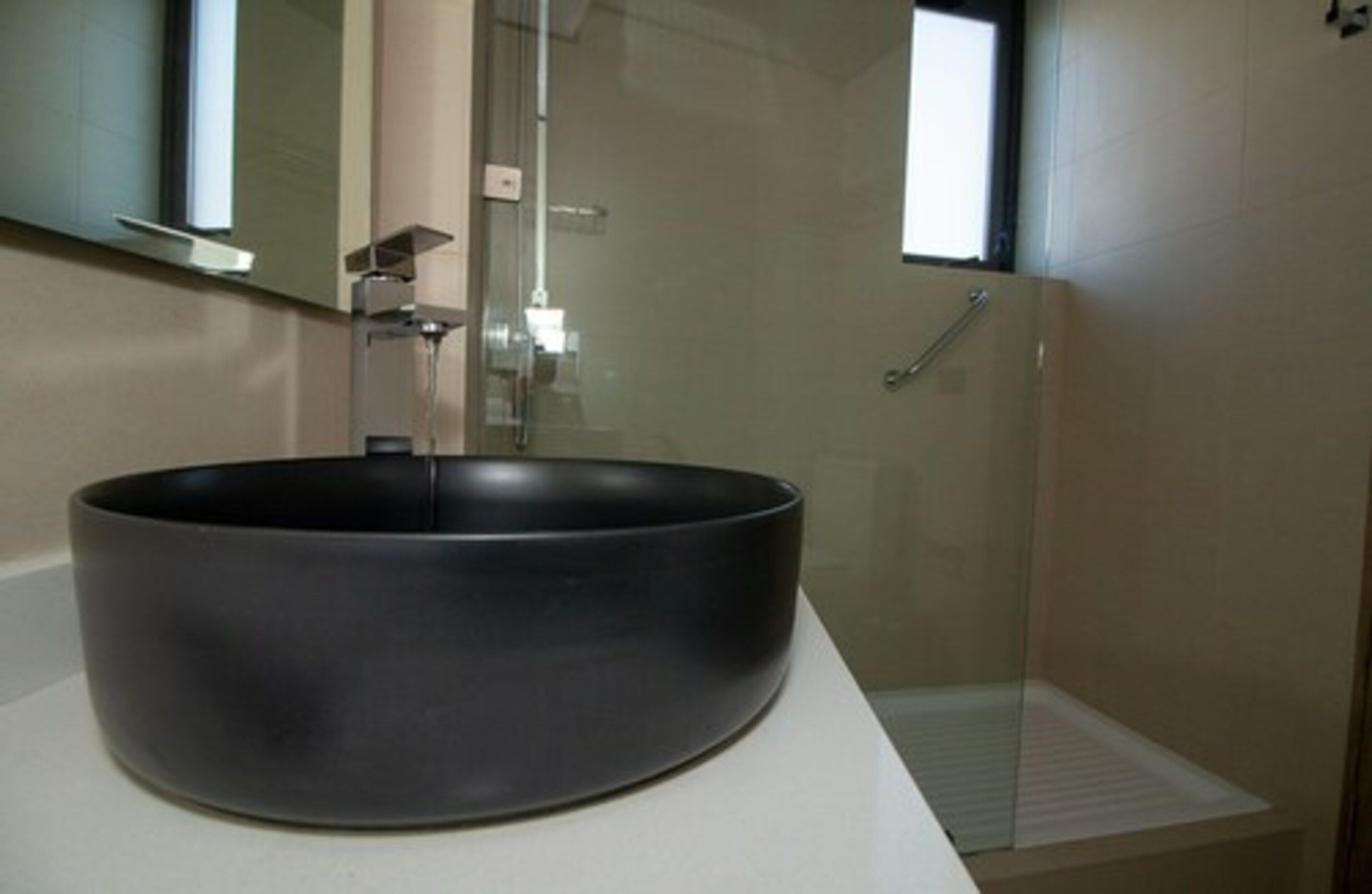 Un bagno moderno con un ampio lavabo nero, cabina doccia in vetro e uno specchio sopra il lavabo.