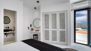 Un dormitorio moderno con una cama grande, un armario con vistas y un baño con un espejo redondo y lavamanos.