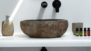 Un baño con un espejo redondo, un lavabo de piedra, un dispensador de jabón y toallas dobladas con esmero.