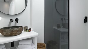 Un baño moderno con tragaluz, espejo redondo, lavamanos grande tipo recipiente y ducha con cerramiento de vidrio.