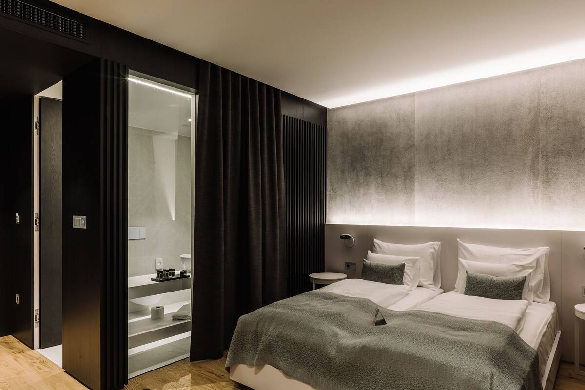 Ein modernes Hotelzimmer mit einem großen Bett, Nachttischen, einem durch eine Glastür einsehbaren Badezimmer und einer strukturierten Wand.