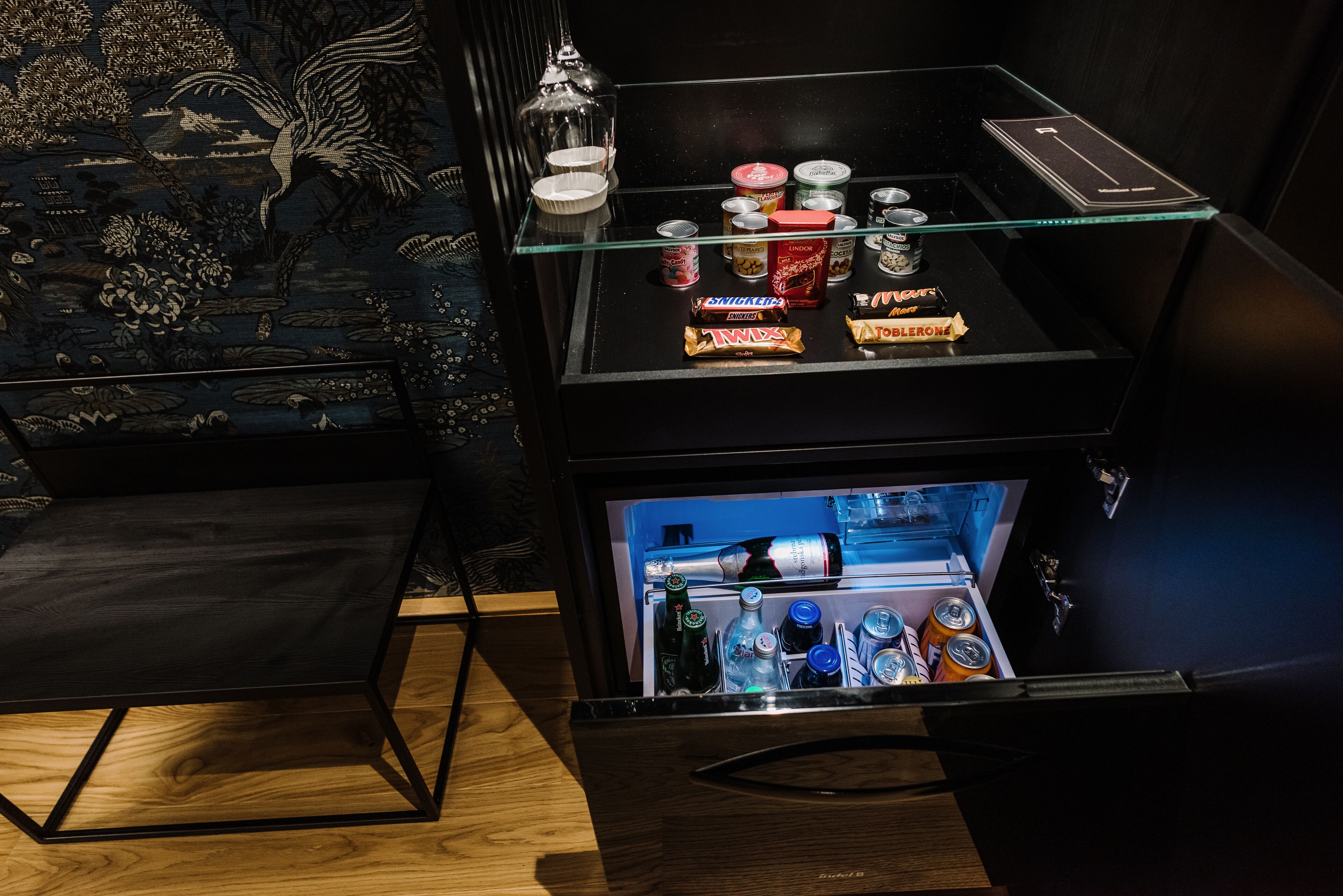 A minibar with snacks and beverages, a glass shelf, and a decorative wall.
