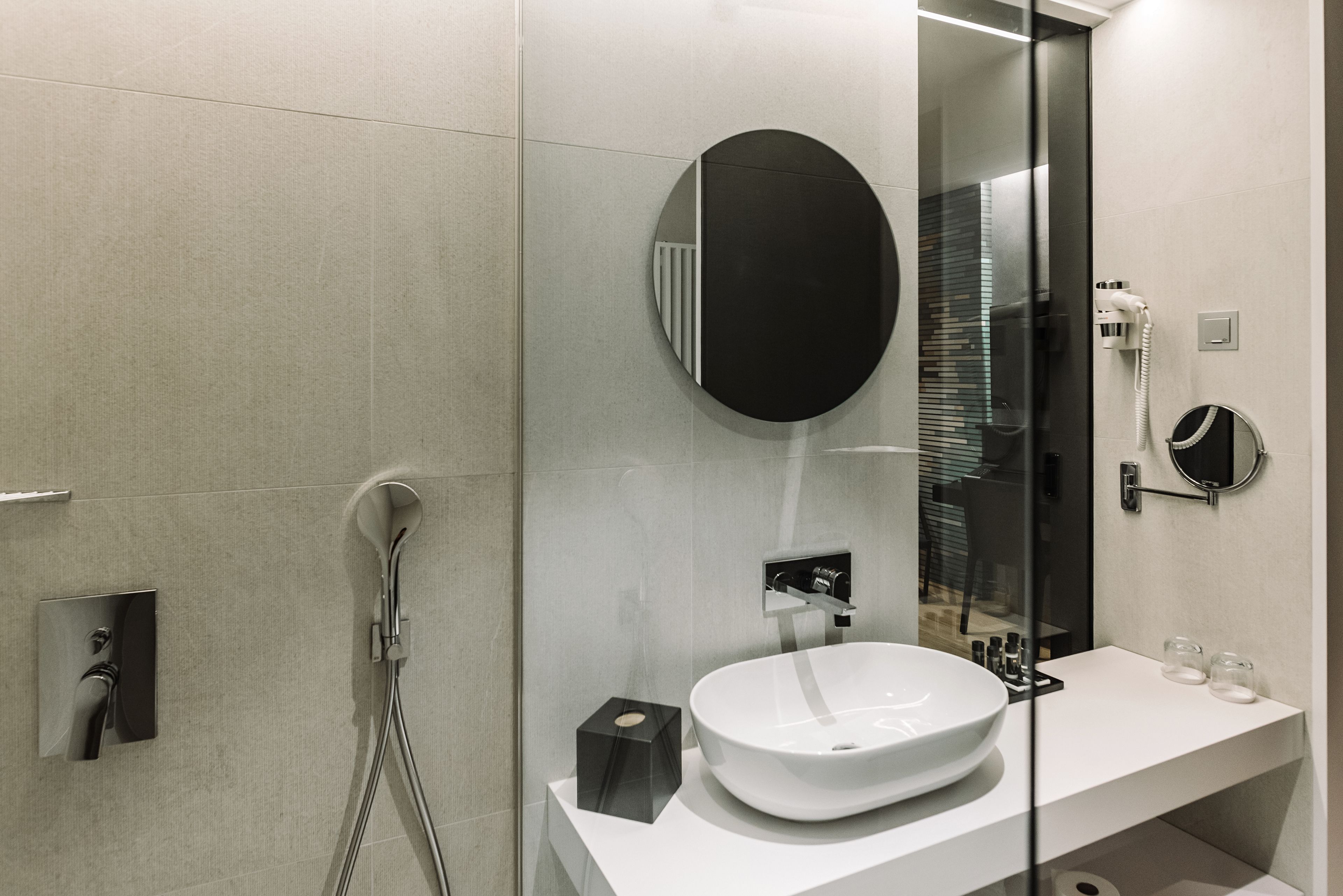 Een moderne badkamer met een witte wastafel, een ronde spiegel en een douchecabine met glazen wanden.