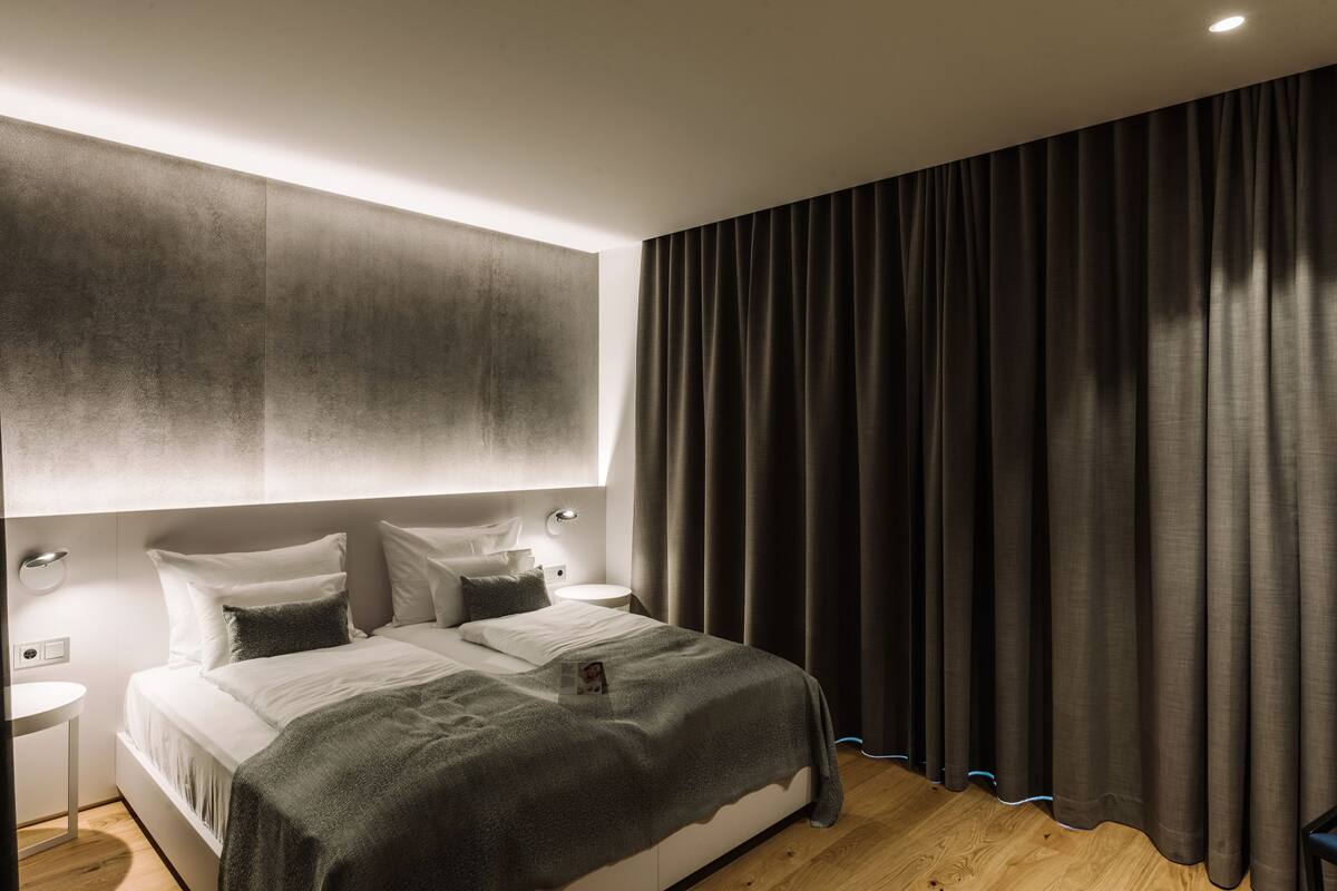 Ein modernes Schlafzimmer mit einem großen Bett, Nachttischen und einem dunklen Vorhang.