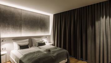 Een moderne slaapkamer met een groot bed, nachtkastjes en een donker gordijn.