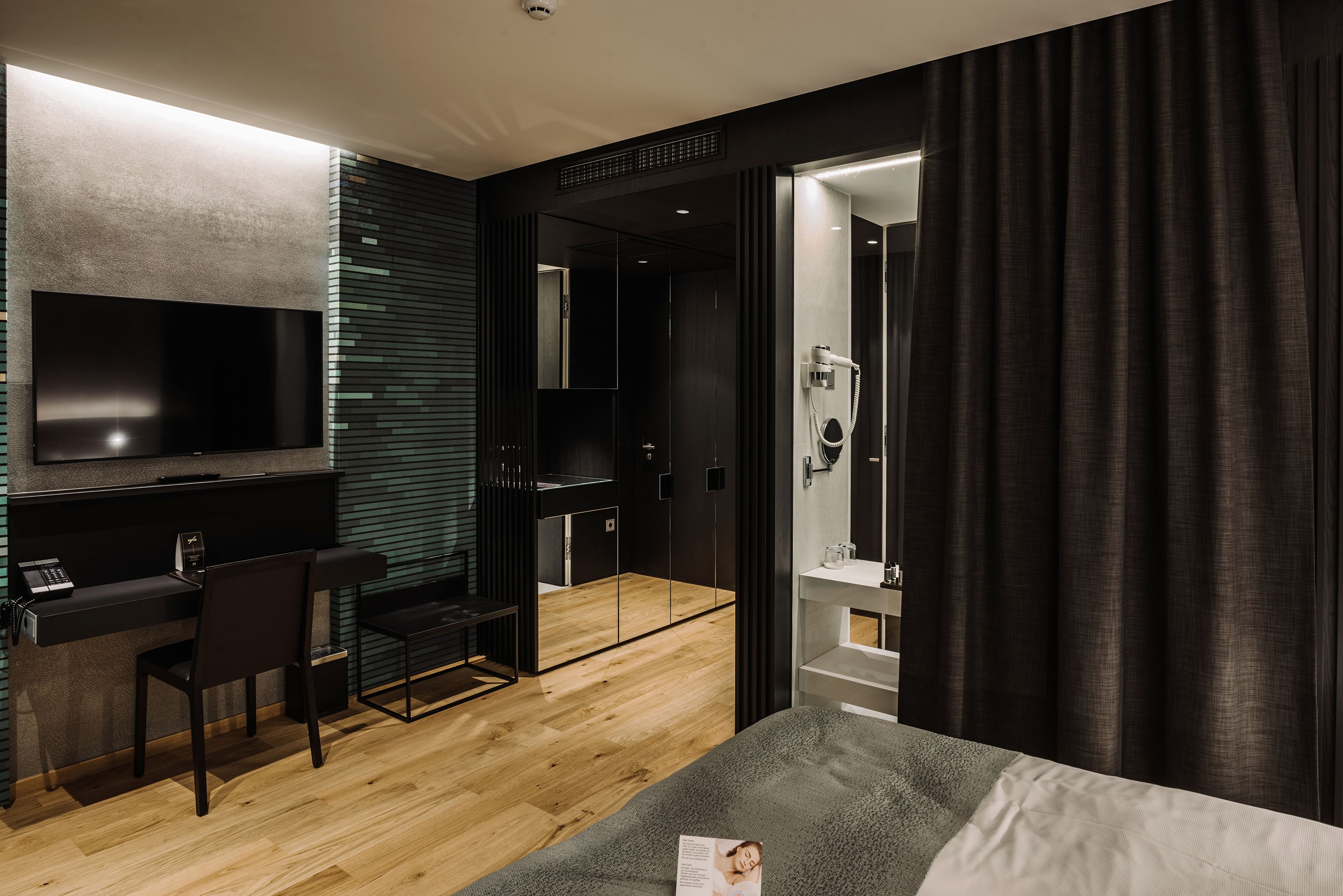 A modern hotel room with a bed, a desk, a chair, a TV, and a shower area.