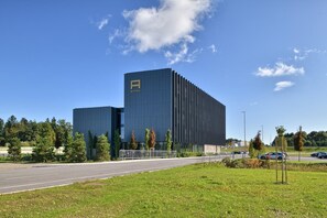 A modern hotel with a prominent 'A' logo, a parking lot, and a clear blue sky. - Hotel A Plus (Zalec)