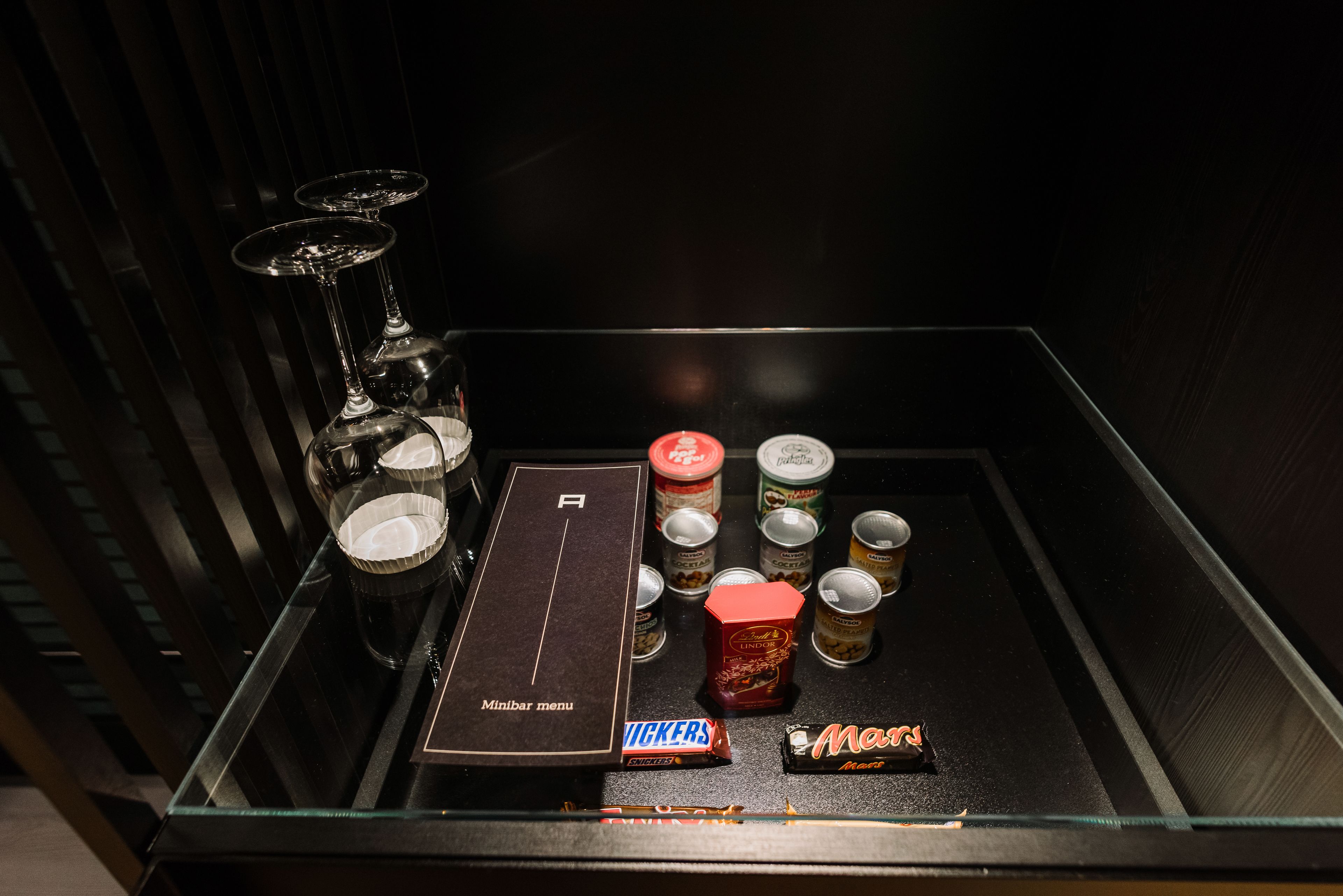 Eine Minibar mit Minibar-Karte, eine Flasche Vickers, eine Mars-Schachtel und mehrere Getränkedosen.