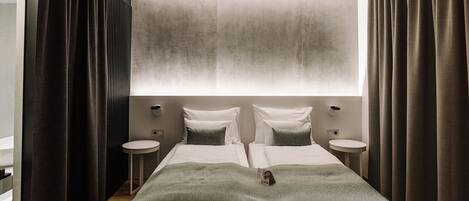 A modern hotel room with a large bed, two bedside tables, and a large window with curtains.