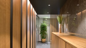 Un área de recepción moderna con un mostrador de madera, una planta en maceta grande y una pared de mármol.