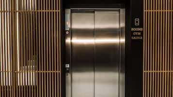 Un ascensor con acabado metálico, un cartel que indica "Habitaciones, Gimnasio, Sauna" y un letrero de "No Fumar."