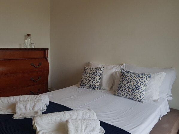 A neatly made bed with white linens and patterned pillows, a wooden dresser with drawers, and a blue throw blanket on the bed. - Olaias Signature Apartment (Lisbon)