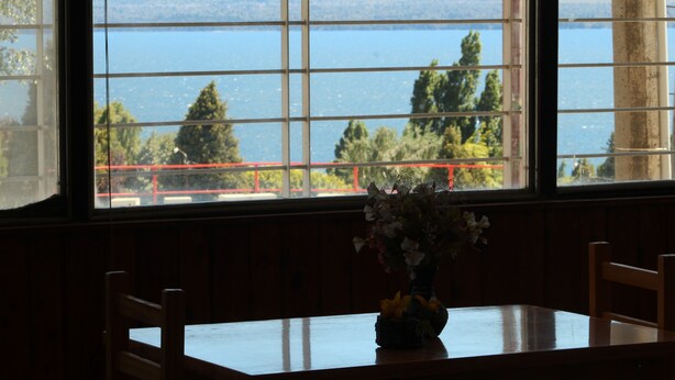 Un tavolo da pranzo con sedie, un vaso con fiori e vista su un lago attraverso una finestra con vetri a griglia.