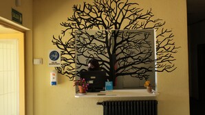Una reception con un grande murale raffigurante un albero, una segnaletica per l'uscita e un erogatore di gel disinfettante.