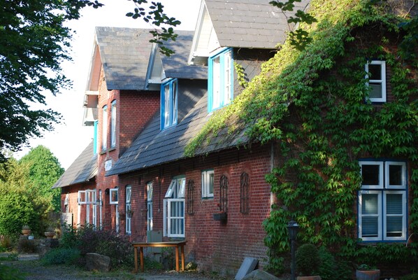 A red brick house with blue shutters, a sloped roof, and ivy growing on the side. - Hotel - Pension ALTES PASTORAT (Langenhorn)