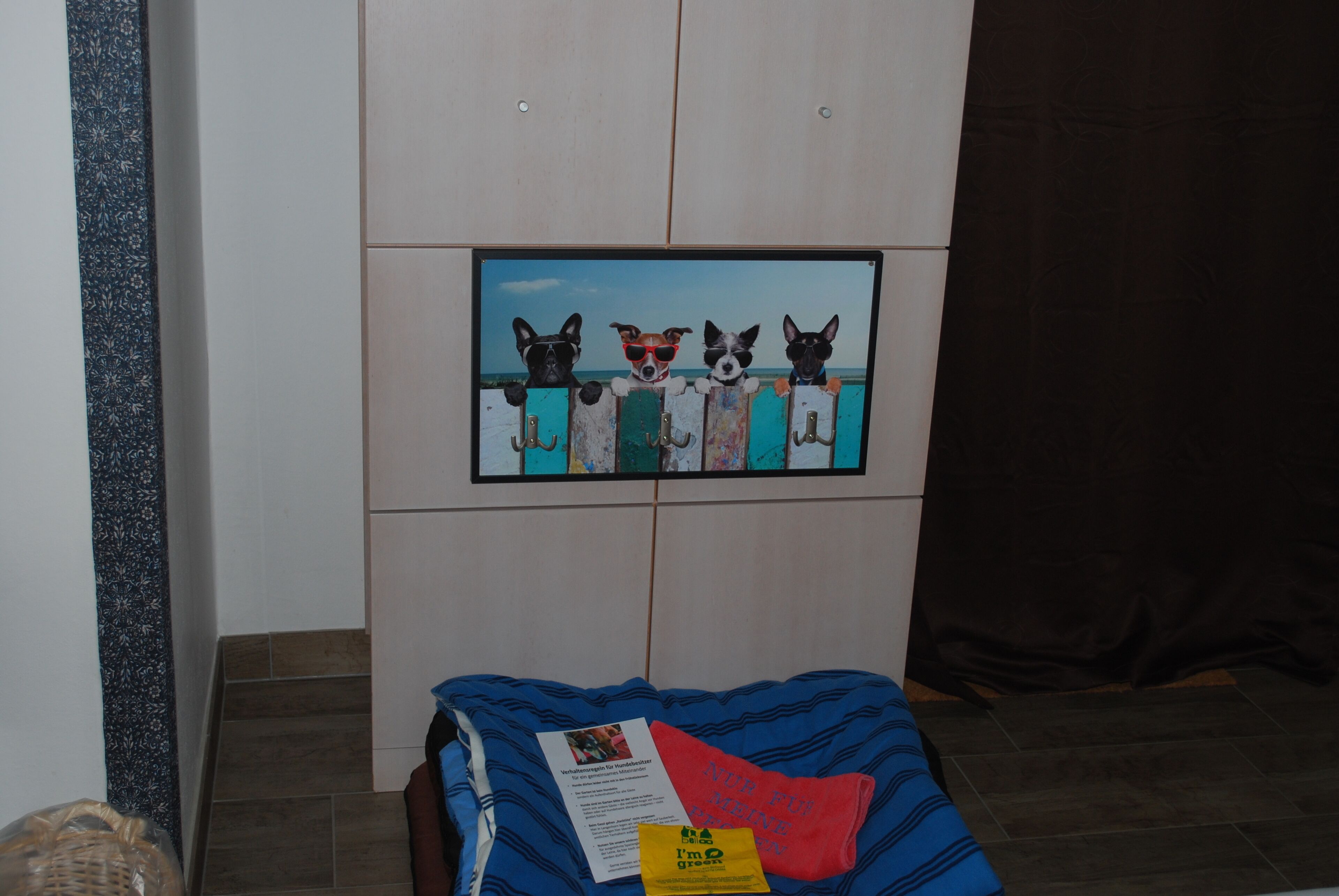 A room with a bed, a framed picture of dogs, and a small sign on the bed.