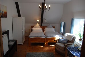 A bedroom with two beds, a wooden wardrobe, a chair, a table, and a chandelier. - Hotel - Pension ALTES PASTORAT (Langenhorn)