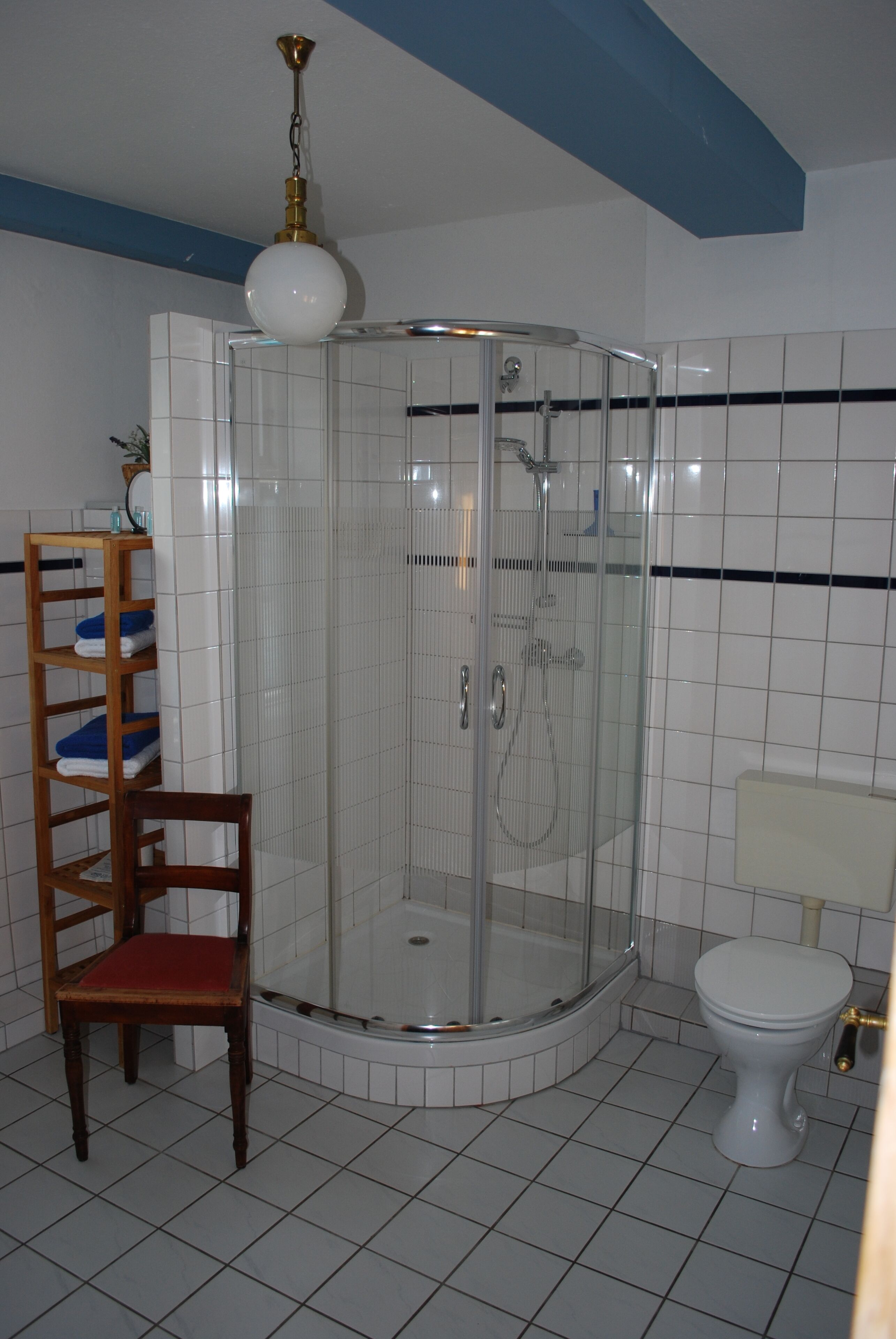 Kylpyhuoneessa on lasiseinällä varustettu suihku, wc ja puinen tuoli.