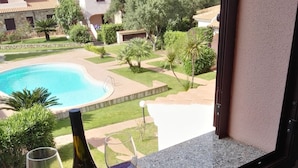 A balcony with a view of a swimming pool, a bottle of wine, and two wine glasses on a mat. - Il Mirto apartment (Monte Petrosu)