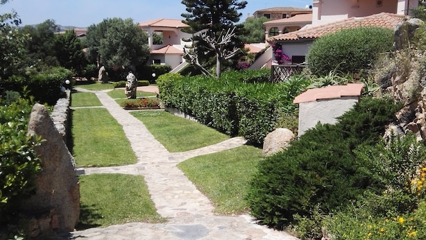 A pathway leading to a residential area with houses, a large tree, and well-maintained gardens. - Il Mirto apartment (Monte Petrosu)