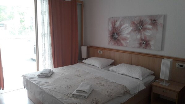 A neatly made bed with white linens and two pillows, a bedside table with a lamp, and a wall with a floral painting.
