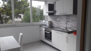 A modern kitchen with white cabinets, a stainless steel sink, and a window overlooking greenery. - Apartments and rooms Marko (Starigrad)