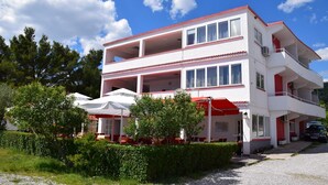 A two-story building with balconies, a covered outdoor seating area, and a car parked in front. - Apartments and rooms Marko (Starigrad)