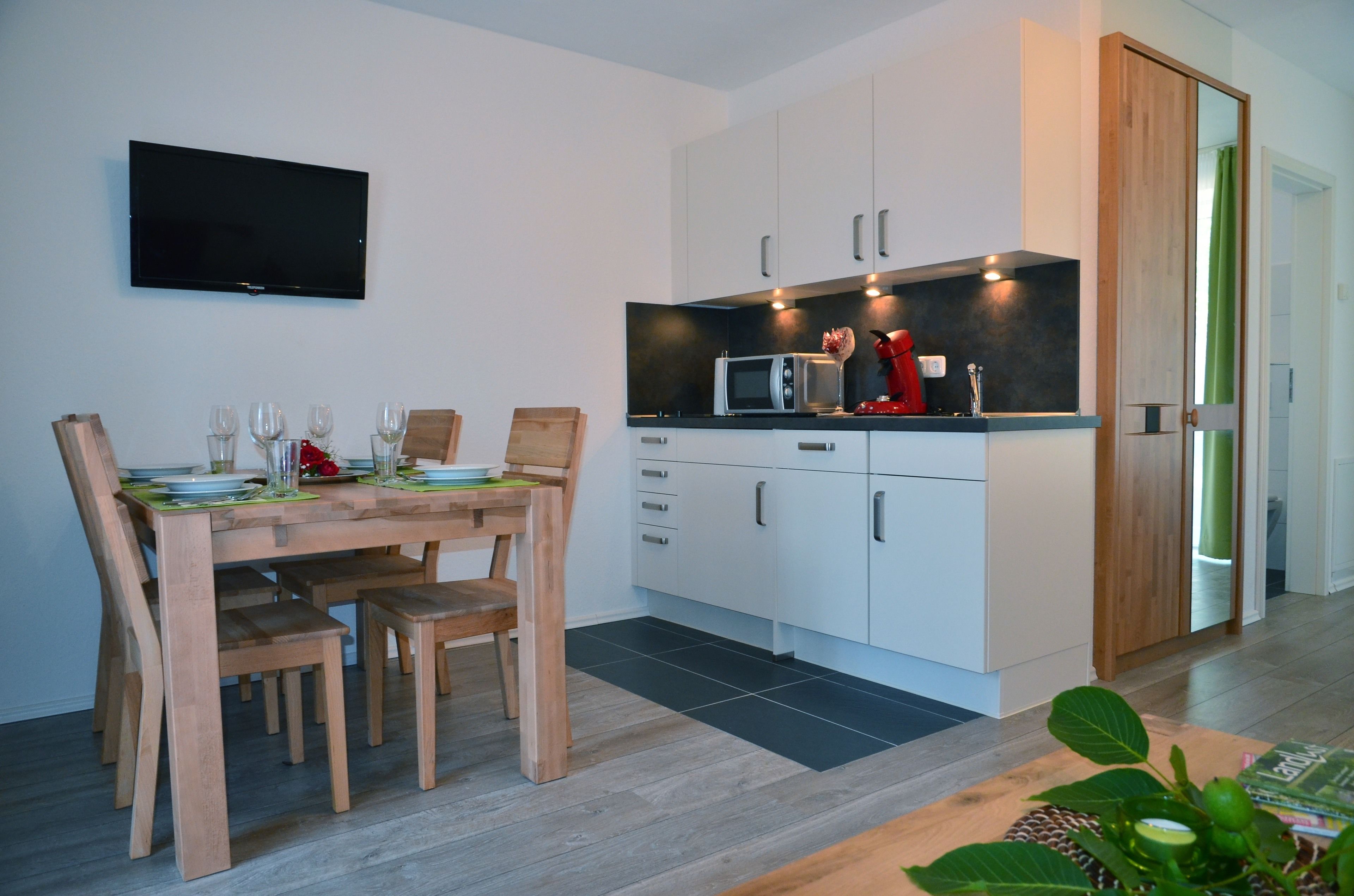 Een moderne keuken met witte kastjes, een magnetron en een televisie aan de muur.