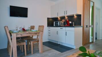 Een moderne keuken met witte kastjes, een magnetron en een televisie aan de muur.