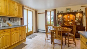 Une cuisine avec des meubles de rangement en bois, une table à manger avec des chaises et une fenêtre avec des rideaux.