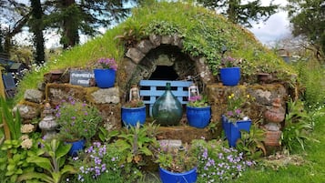 Una construcción rústica de piedra con techo cubierto de musgo, rodeada de macetas con plantas y flores.