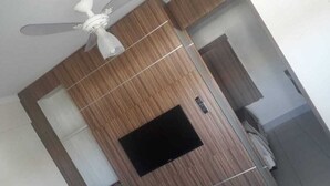A room with a ceiling fan, a wooden panel wall, a black TV screen, and a door. - Lacqua di Roma (Caldas Novas)