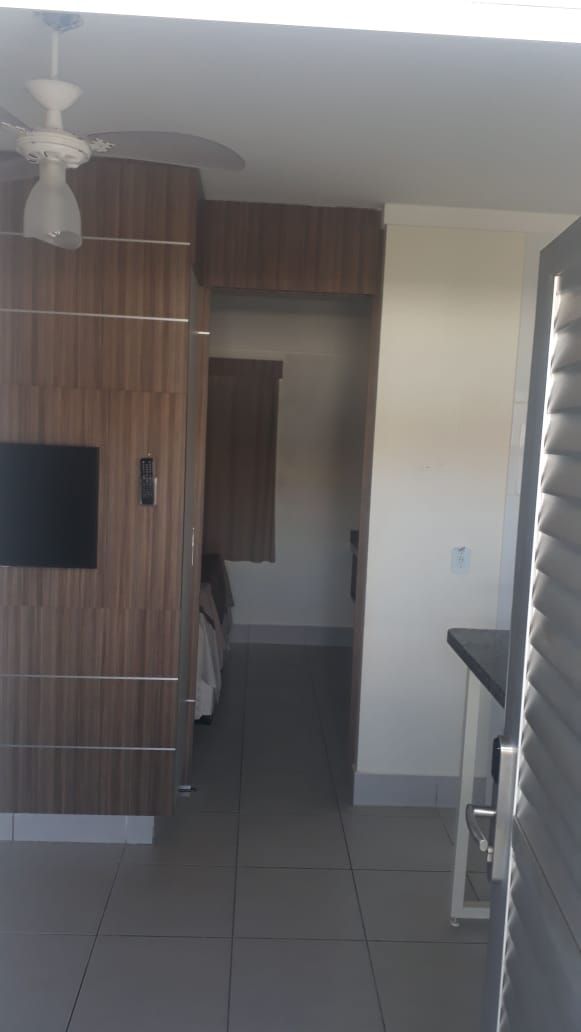 A hallway with a ceiling fan, a wooden wall panel, a door with a handle, and a small shelf.