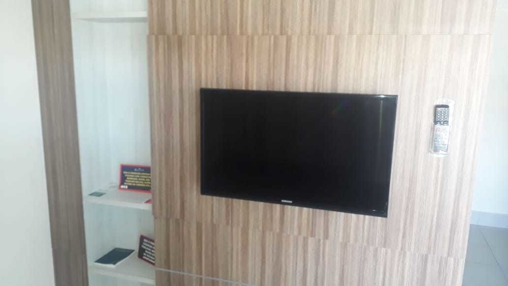 Un téléviseur à écran plat fixé à un mur en bois, avec une télécommande posée sur une étagère en dessous.