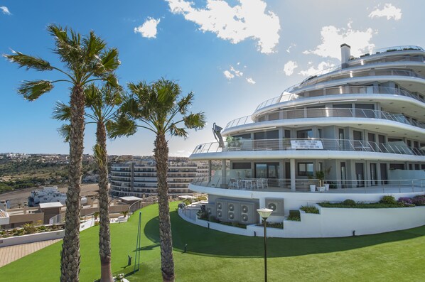 Un hotel de varios pisos con fachada curva, mobiliario exterior y palmeras.