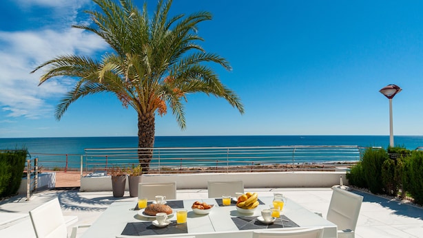 A table set for breakfast with a view of the sea, a palm tree, and a lifeguard tower. - Myflats Infinity View (Elche)
